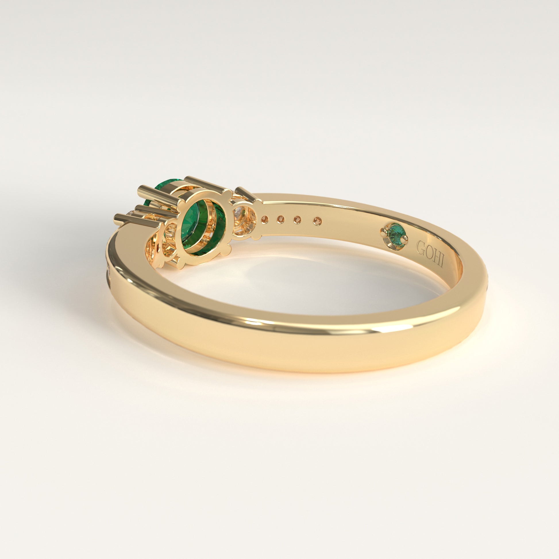 back view of a Trilogy Ring crafted in 18k yellow gold — a round green Colombian emerald at the center, flanked by two round diamonds, with smaller diamonds set along both shoulders.