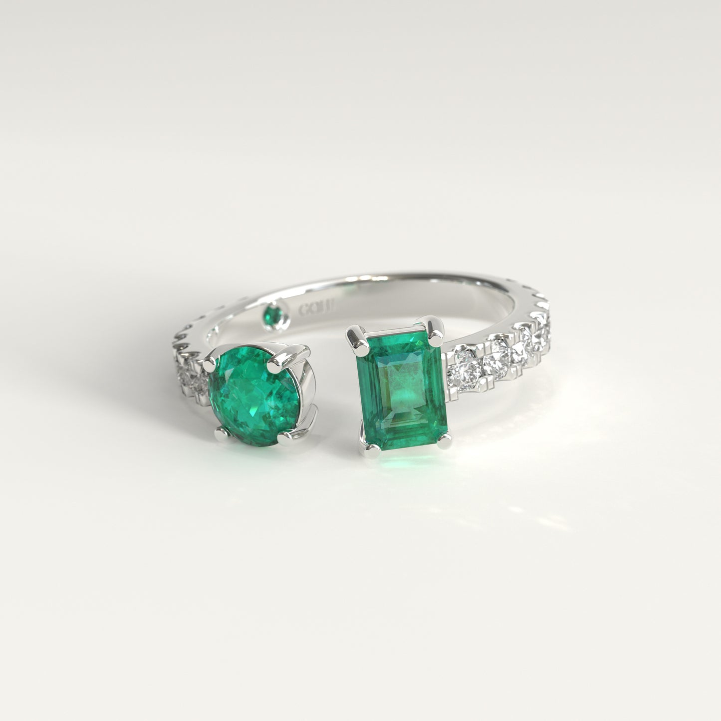 Duet Ring in 18k white gold, Colombian emerald and diamond toi et moi ring, Soiree Collection by GOHI. A 18k fairmined white gold ring featuring two colombian emeralds one, emerald-cut, and one round cut, set in a band adorned with small clear stones, photographed on a clean white background. 
