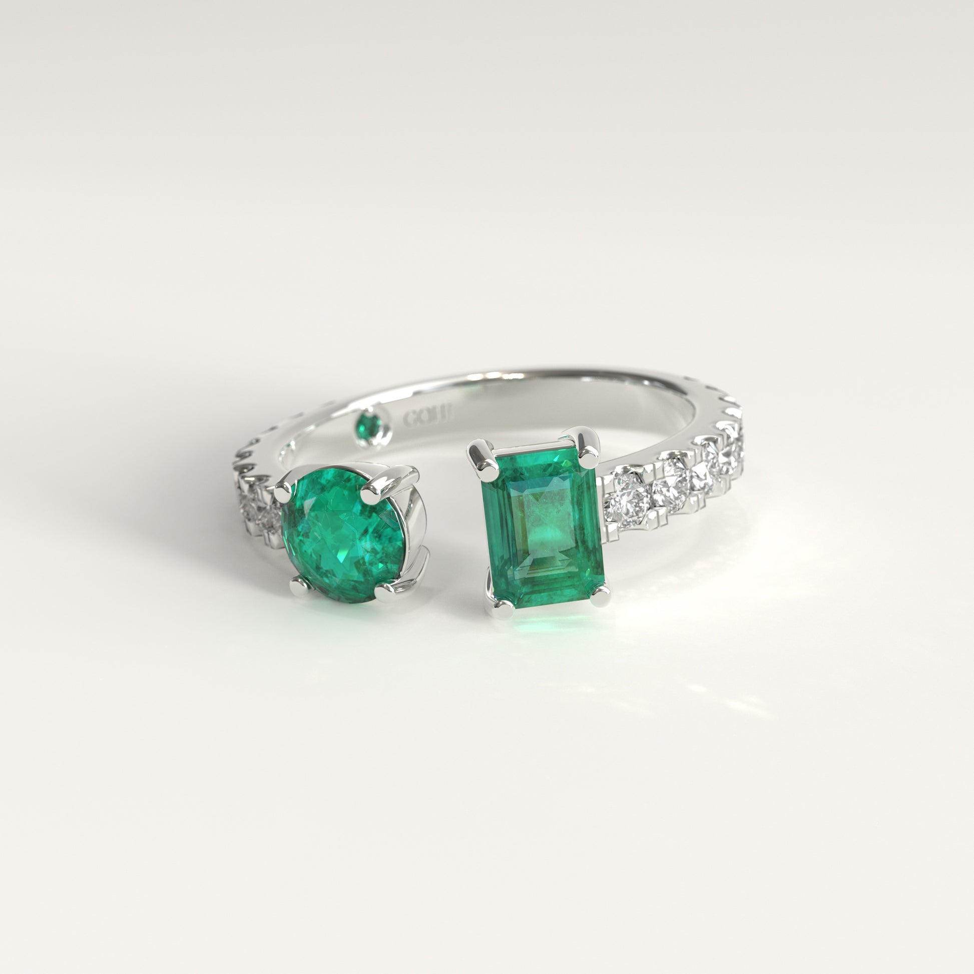 Duet Ring in 18k white gold, Colombian emerald and diamond toi et moi ring, Soiree Collection by GOHI. A 18k fairmined white gold ring featuring two colombian emeralds one, emerald-cut, and one round cut, set in a band adorned with small clear stones, photographed on a clean white background. 