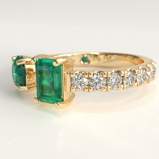 Close-up of round and emerald-cut Colombian emeralds on open toi et moi ring, Duet Ring by GOHI Soiree Collection. A 18k fairmiend yellow gold ring featuring a large rectangular emerald-cut Colombian emerald gemstone, a smaller round emerald-cut colombian emerald on the opposite side, and a row of round brilliant-cut diamonds along the band.