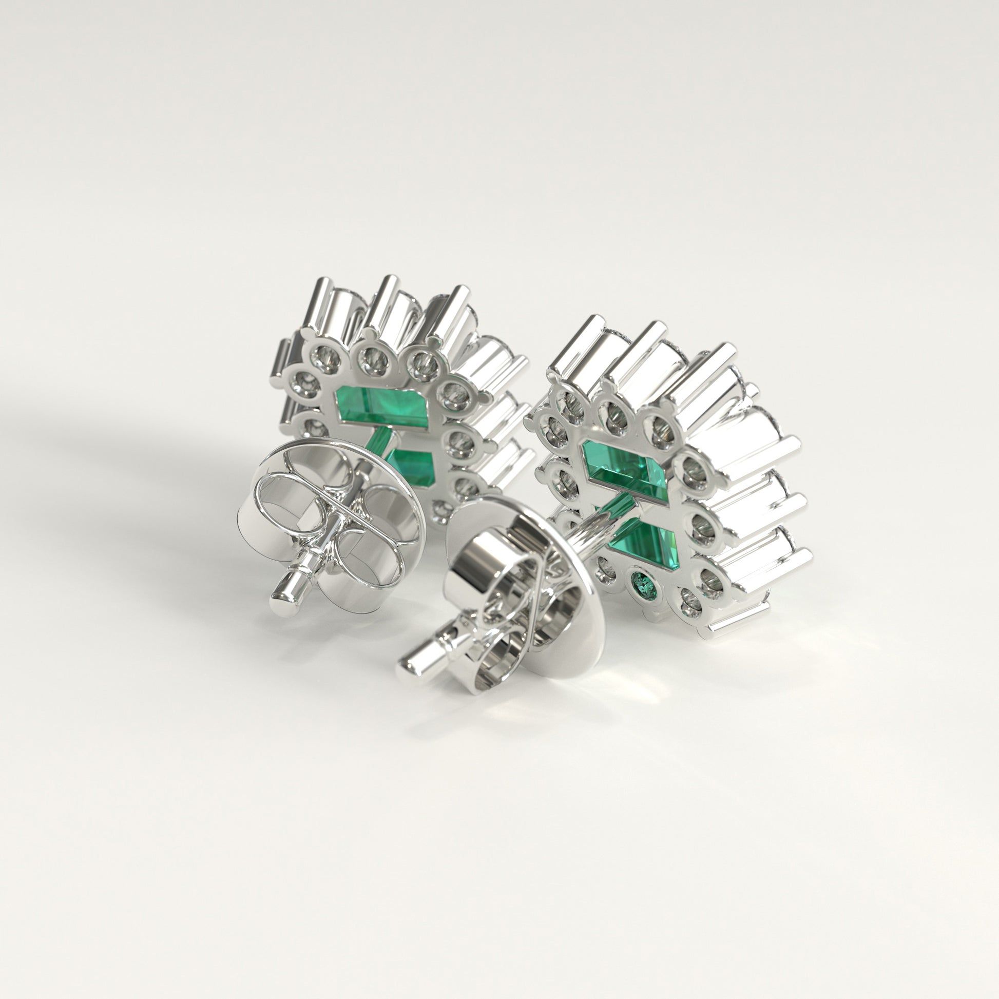 Back  view of a pair of white gold stud earrings with a textured, geometric design featuring small diamonds and rectangular colombian emerald inset accents, displayed on a clean light gray background.