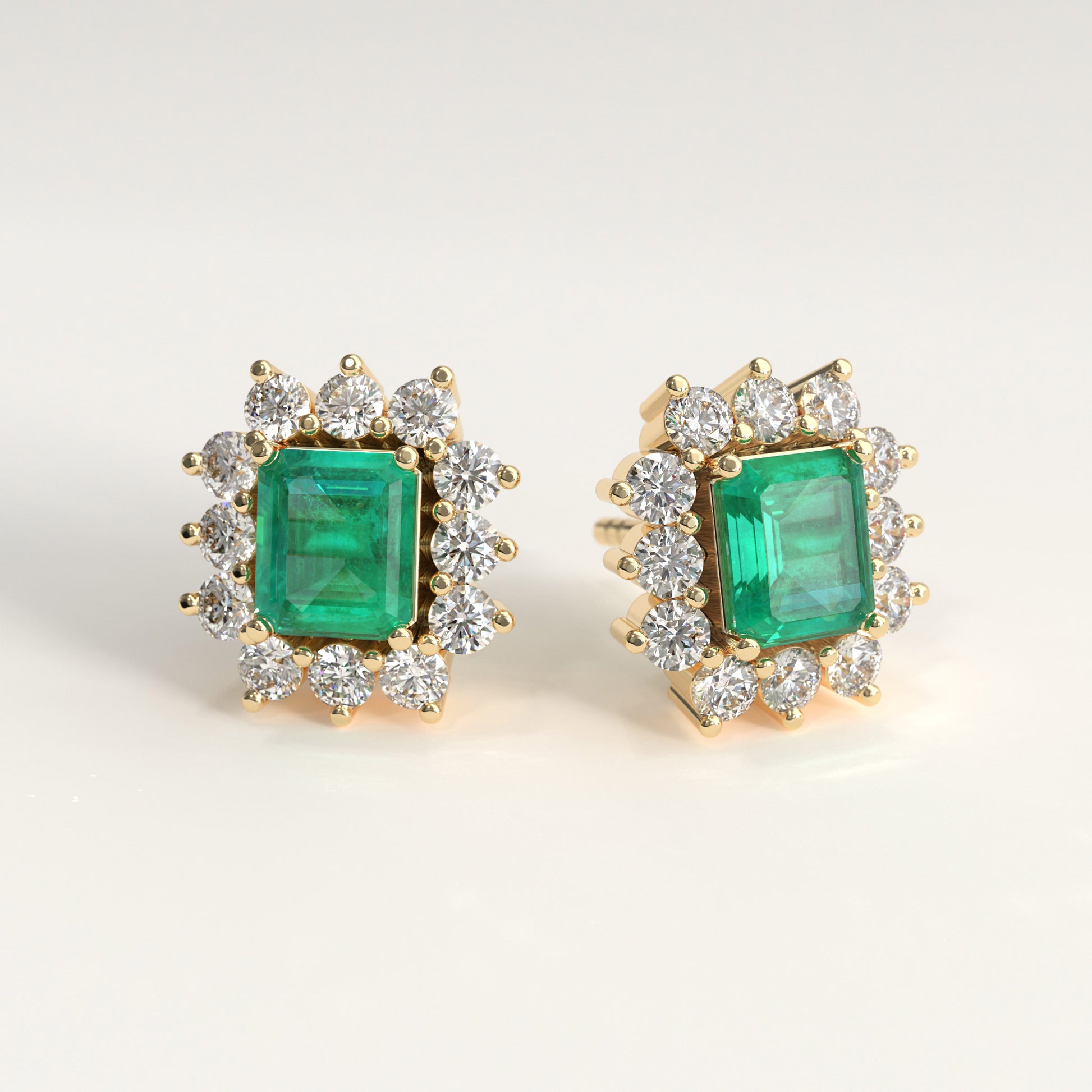 A pair of 18k fairmined yellow gold stud earrings featuring a central emerald-cut colombian emerald surrounded by a halo of small diamonds round-cut, set against a plain light background.