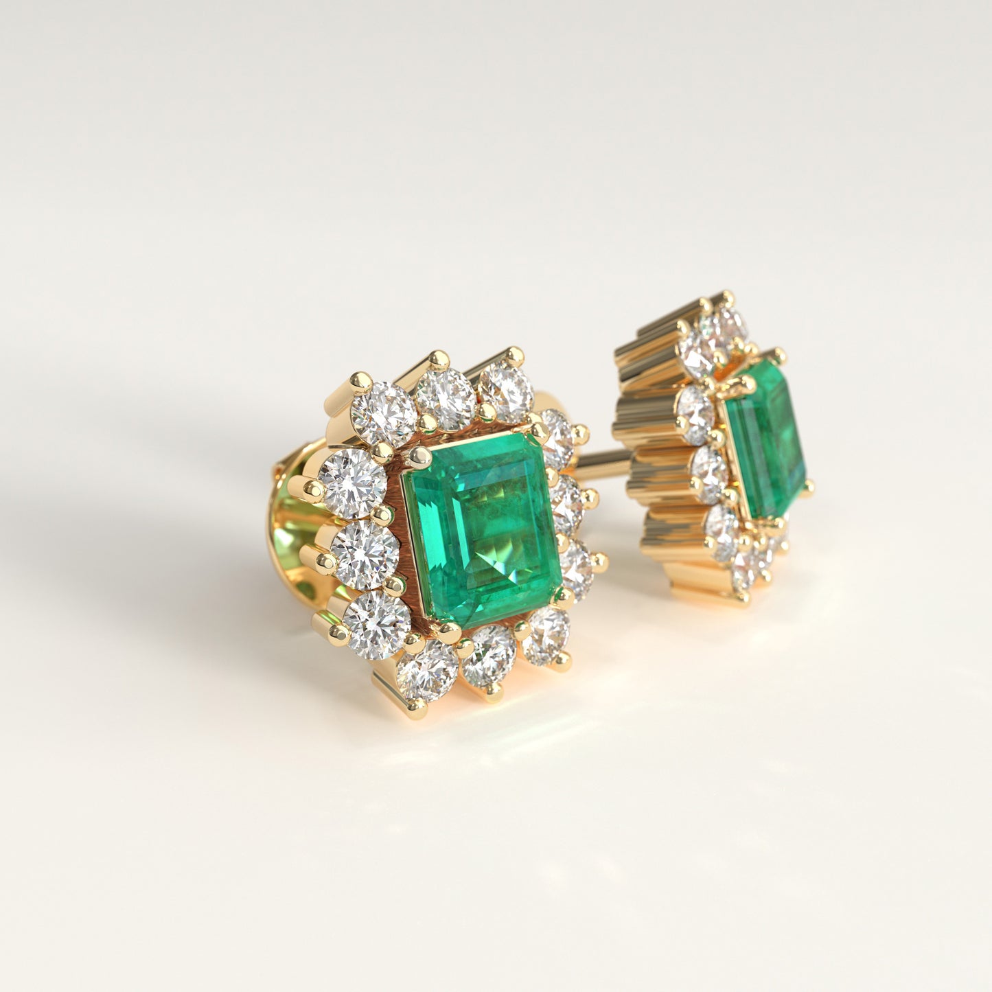 Lateral view of a pair of yellow gold stud earrings featuring a central rectangular colombian emerald emerald-cut surrounded by small round diamonds, photographed on a clean light background.
