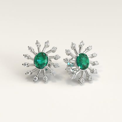 A pair of White gold starburst stud earrings, each featuring a oval colombian emerald center stone surrounded by smaller natural diamonds, shown on a light beige background.