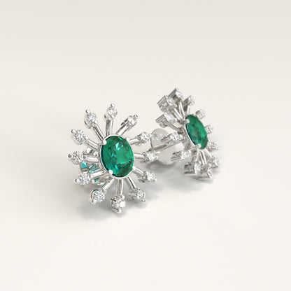 A pair of White gold stud earrings featuring oval colombian emerald center surrounded by radiating diamonds clusters, photographed on a clean light gray background.