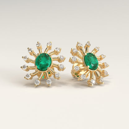 Nova Earrings in 18k yellow gold — Colombian emerald and diamond burst stud earrings, Soiree Collection by GOHI. A pair of 18k yellow gold starburst stud earrings, each featuring a central oval colombian emerald stone surrounded by smaller round diamonds, shown on a light beige background.