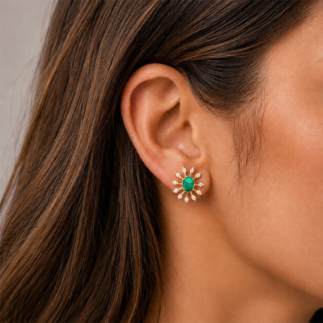 A close-up of a woman's ear wearing a small gold flower-shaped stud earring with a green center and diamondspetals.